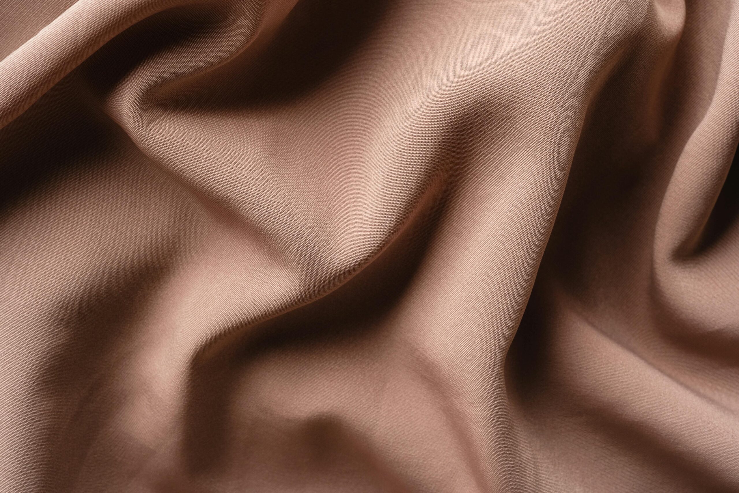 Smooth brown satin fabric with gentle wrinkles creating a wavy texture. Ideal for design and fashion concepts.